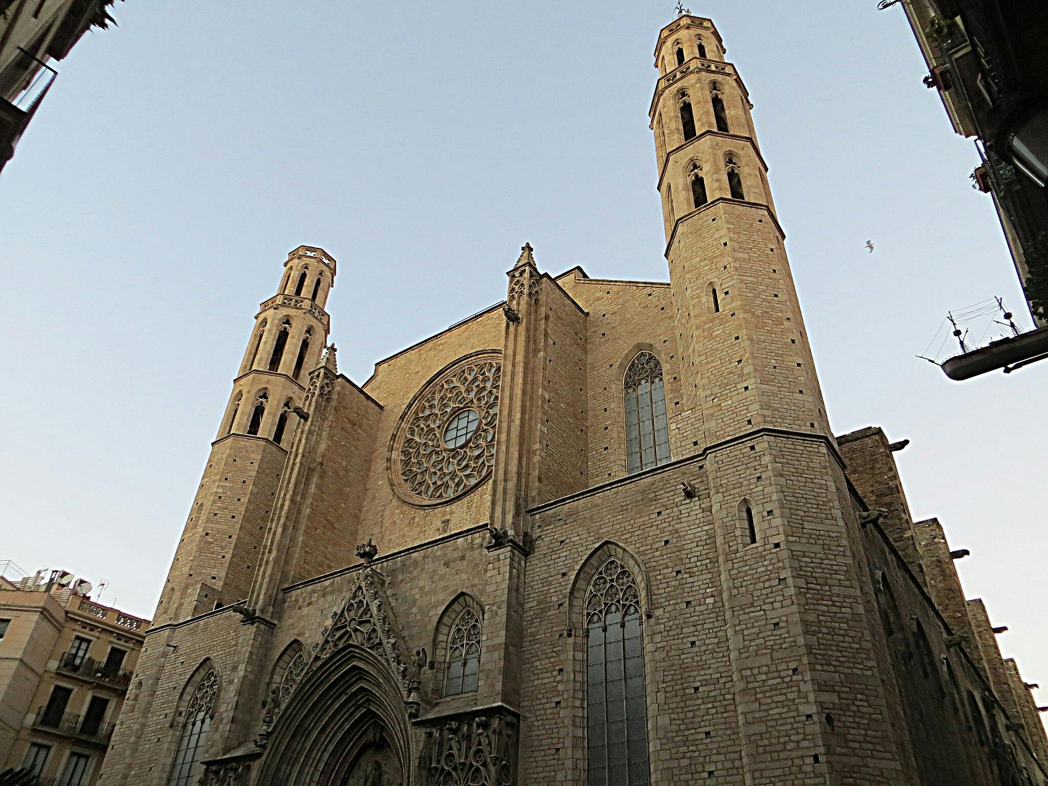 Grande église gothique en pierre avec deux clochers, une grande rosace et une entrée en arc brisé sur fond de ciel clair.
