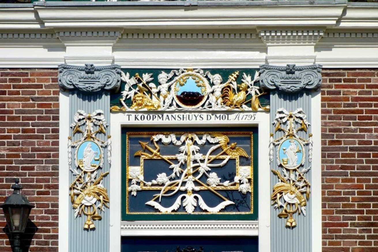 複雑な彫刻、柱、金色のアクセントが施された華やかなファサード。 刻印には「T KOOPMANSHUYS D'MOL 1795」と書かれています。