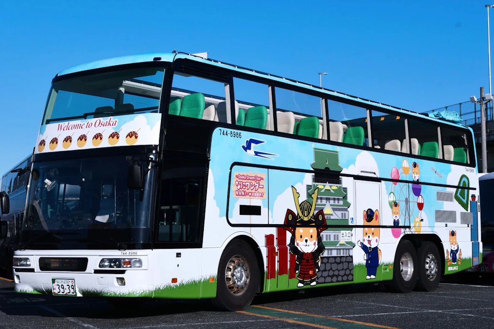 A colorful double-decker bus with cartoon characters and a castle illustration on its side, parked in a sunny area.