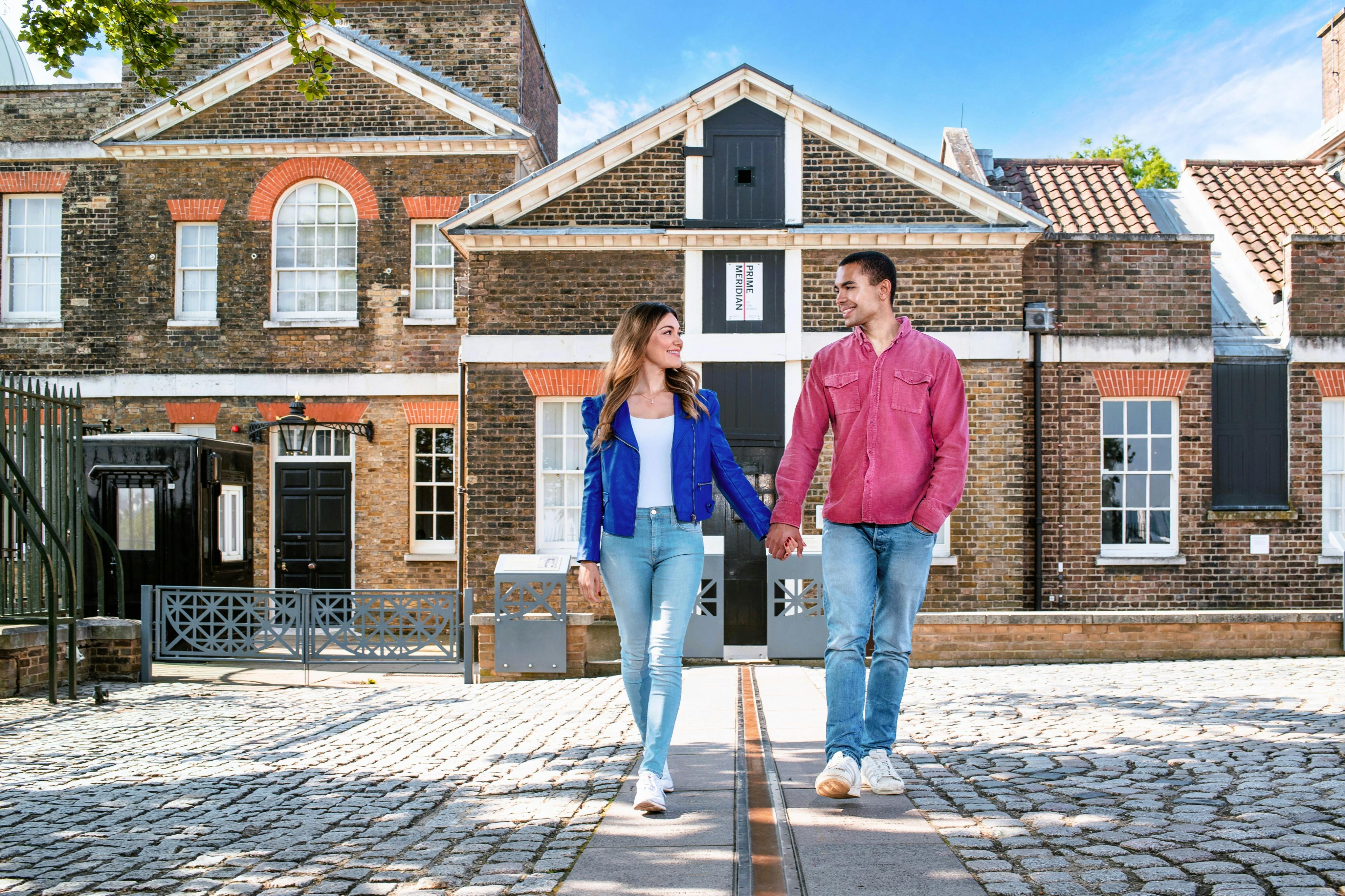 Para trzyma się za ręce, idąc brukowaną ścieżką przed zabytkowym, ceglanym budynkiem pod czystym, błękitnym niebem.