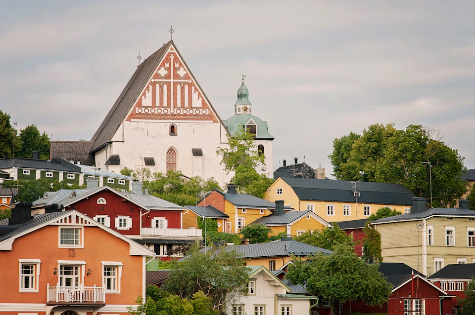 Colorful houses and a historic church with a steep roof and ornate design, surrounded by greenery under a cloudy sky.