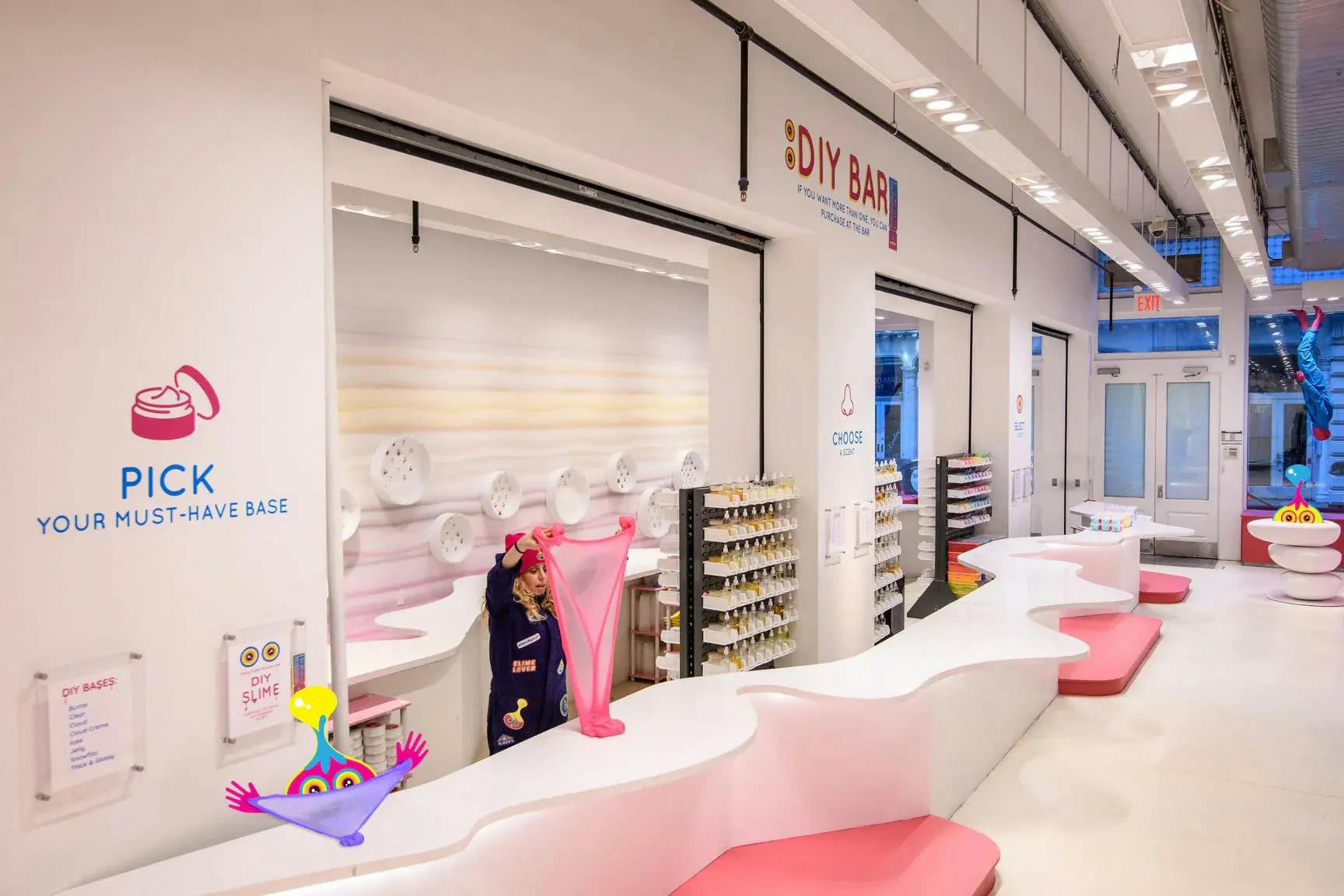 Dítě protahuje růžový sliz u barového pultu pro kutily s policemi z řemeslných materiálů uvnitř jasně osvětleného moderního prostoru.