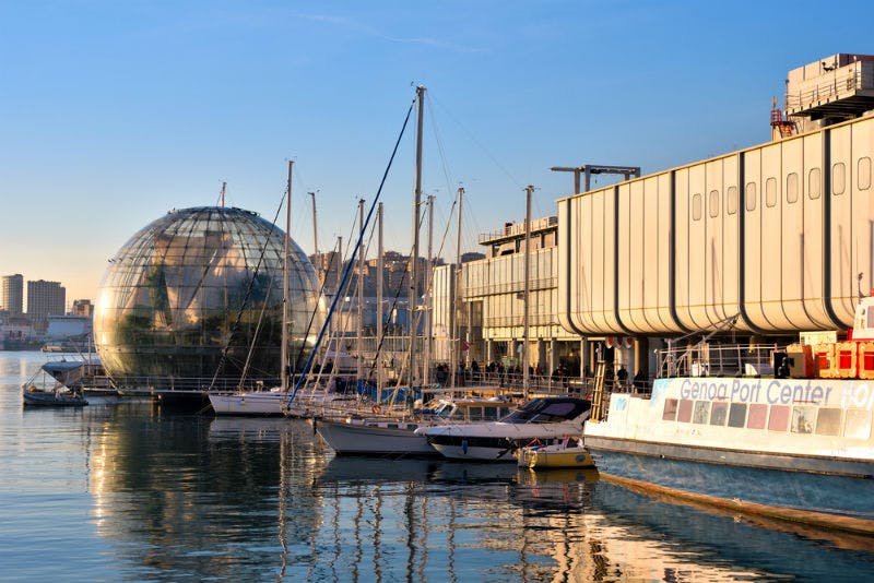 船只停靠在现代建筑和玻璃穹顶结构旁边的港口，平静的水反映出场景。