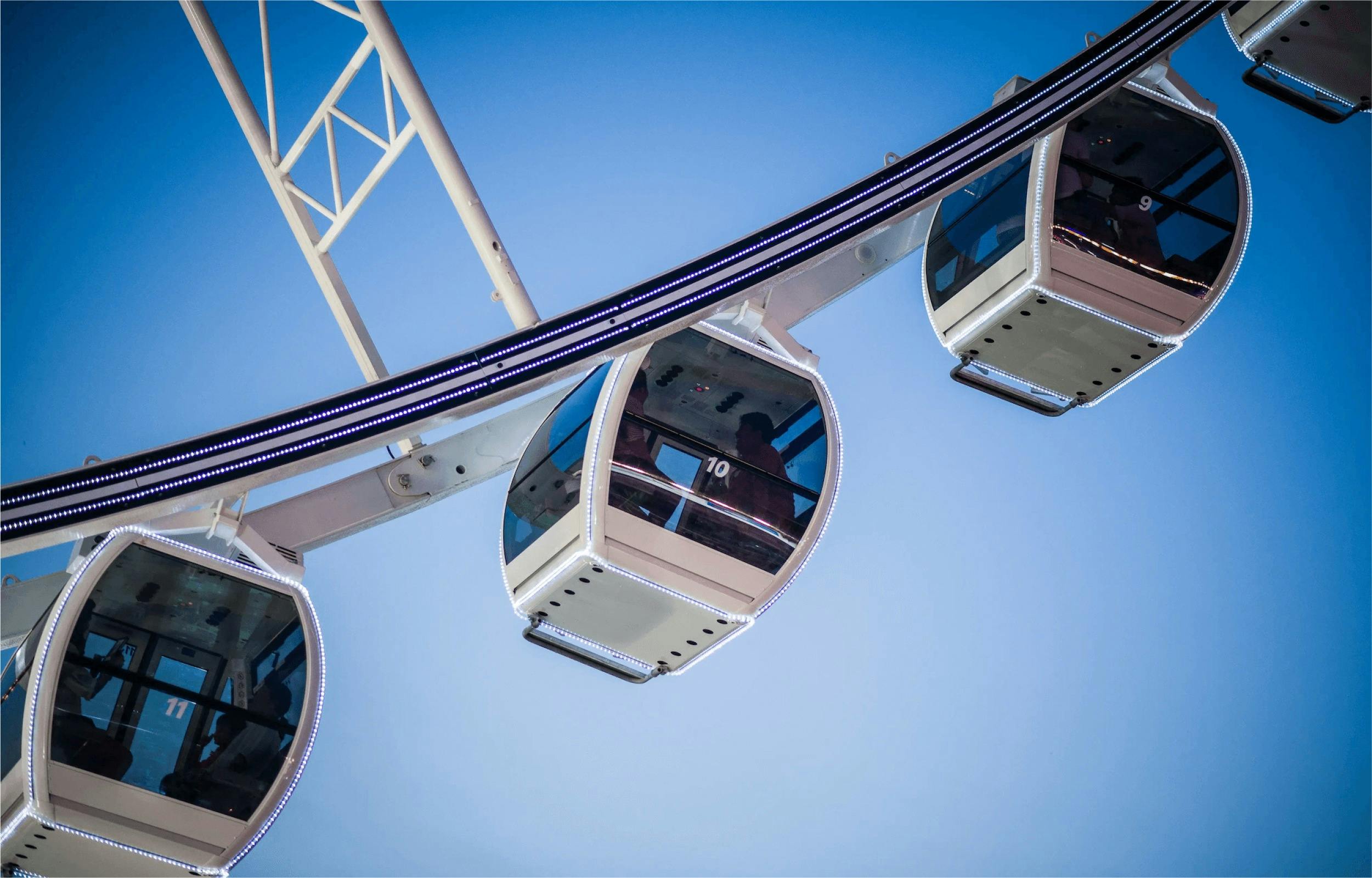 Close-up of three Ferris wheel cabins against a blue sky, with one visible occupant inside the middle cabin.