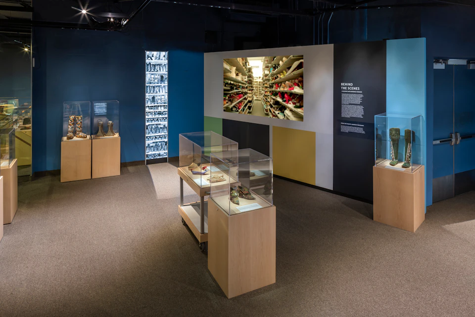 Museum exhibit with various artifacts in glass cases, a large central photo display, and informational text on the wall.