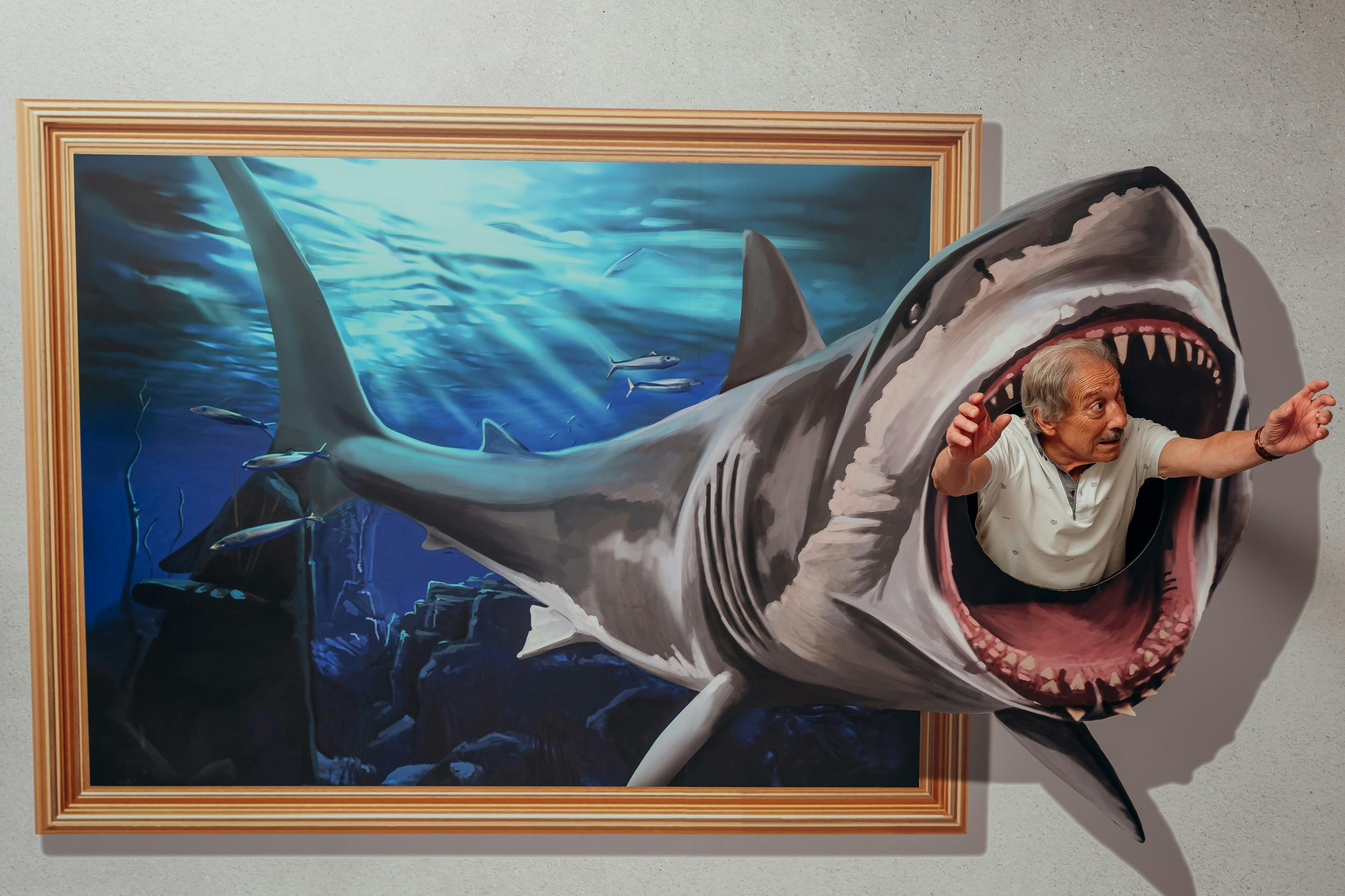 Un homme semble sortir de la gueule ouverte d'un requin peint en 3D sur un mur, créant ainsi l'illusion d'être dévoré.
