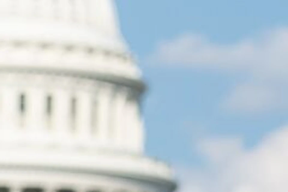 Three people converse and smile in front of the United States Capitol building on a sunny day.