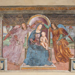 A woman sitting with a child on her lap is crowned by two angels under a decorative ceiling.