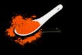 Curry powder on white spoon against black background.