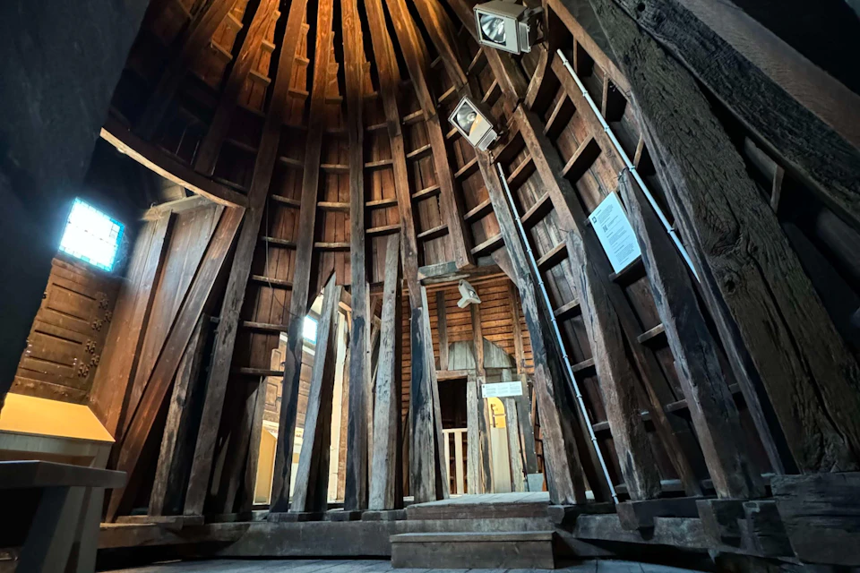 Interior of a wooden structure with tall beams, a vaulted ceiling, and lighting fixtures illuminating the space.
