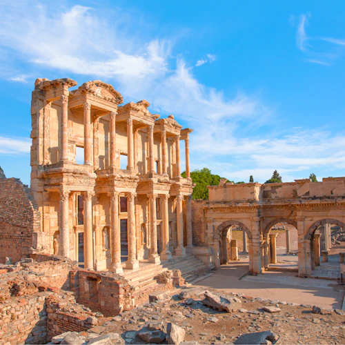 Forntida stenruiner med invecklade pelare och valv under en klarblå himmel, omgiven av utspridda stenar och halvväggar.