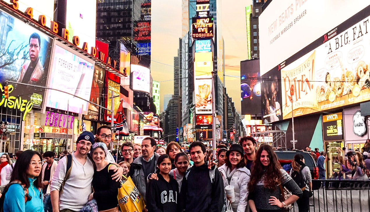 A group of people smiling and posing for a picture in a bustling, brightly lit commercial area with many billboards, likely Times Square.