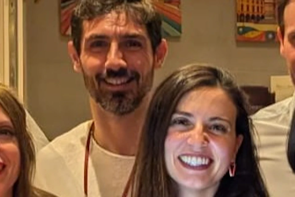 A group of people smiling together behind a bar-style table with tablets. Art hangs on the walls, and hanging lights illuminate the scene.