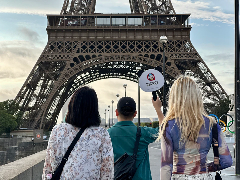 Three people facing the Eiffel Tower; one holds a panda sign.