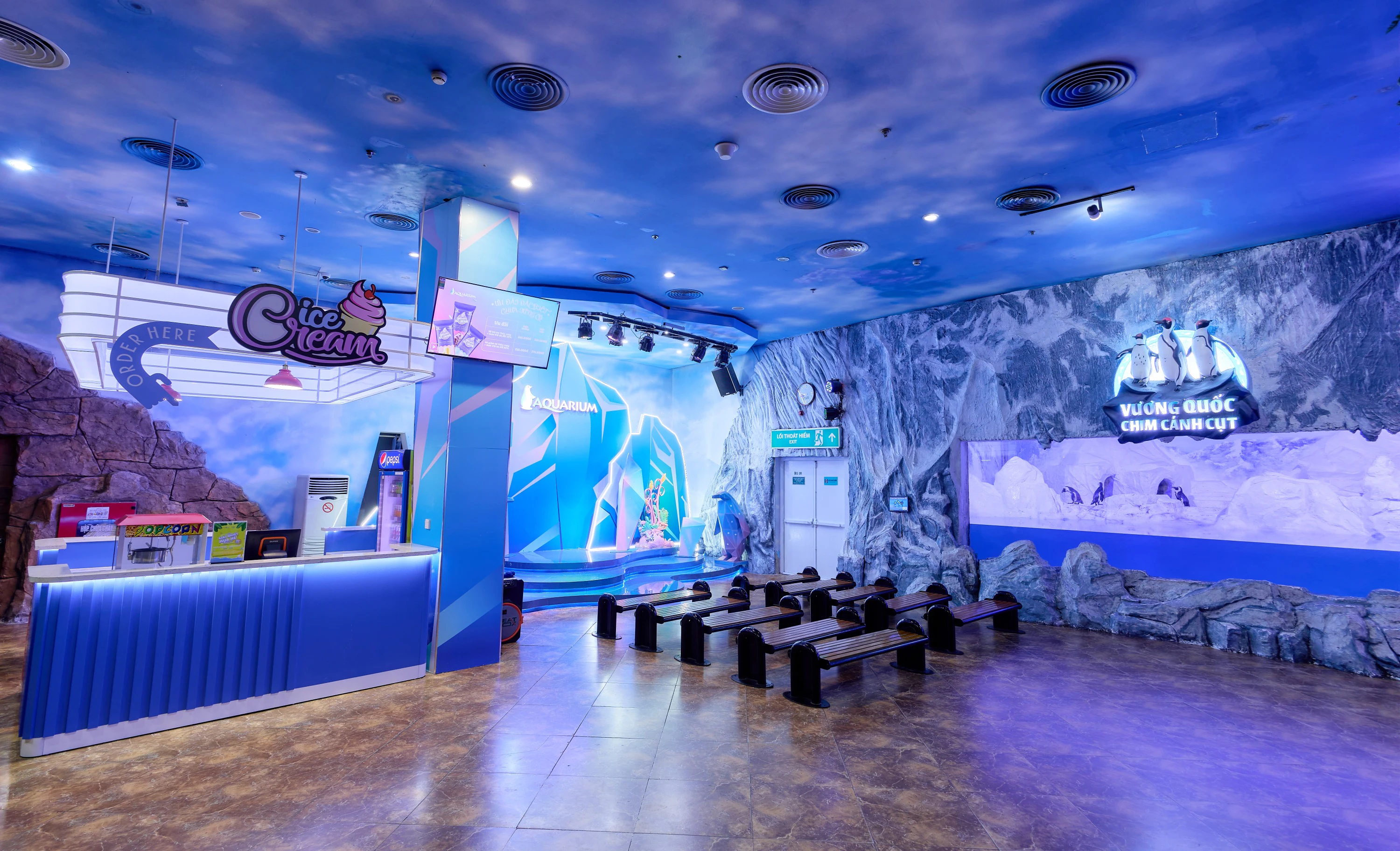 An indoor aquarium-themed space with blue walls, seating, and an ice cream counter under a sky-like ceiling.