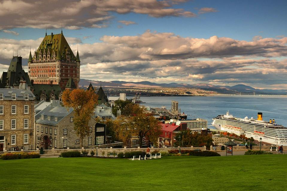 A scenic view of Château Frontenac, a waterfront area, and a cruise ship docked under a partly cloudy sky.