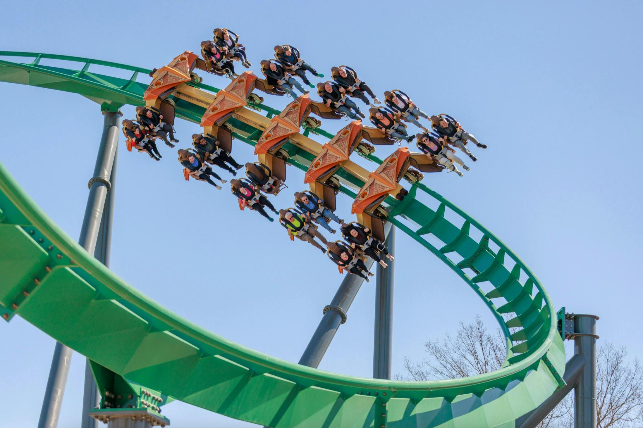Американские горки с зелеными гусеницами и оранжевыми машинами, перевозящие всадников вверх ногами по петле под ясным голубым небом.