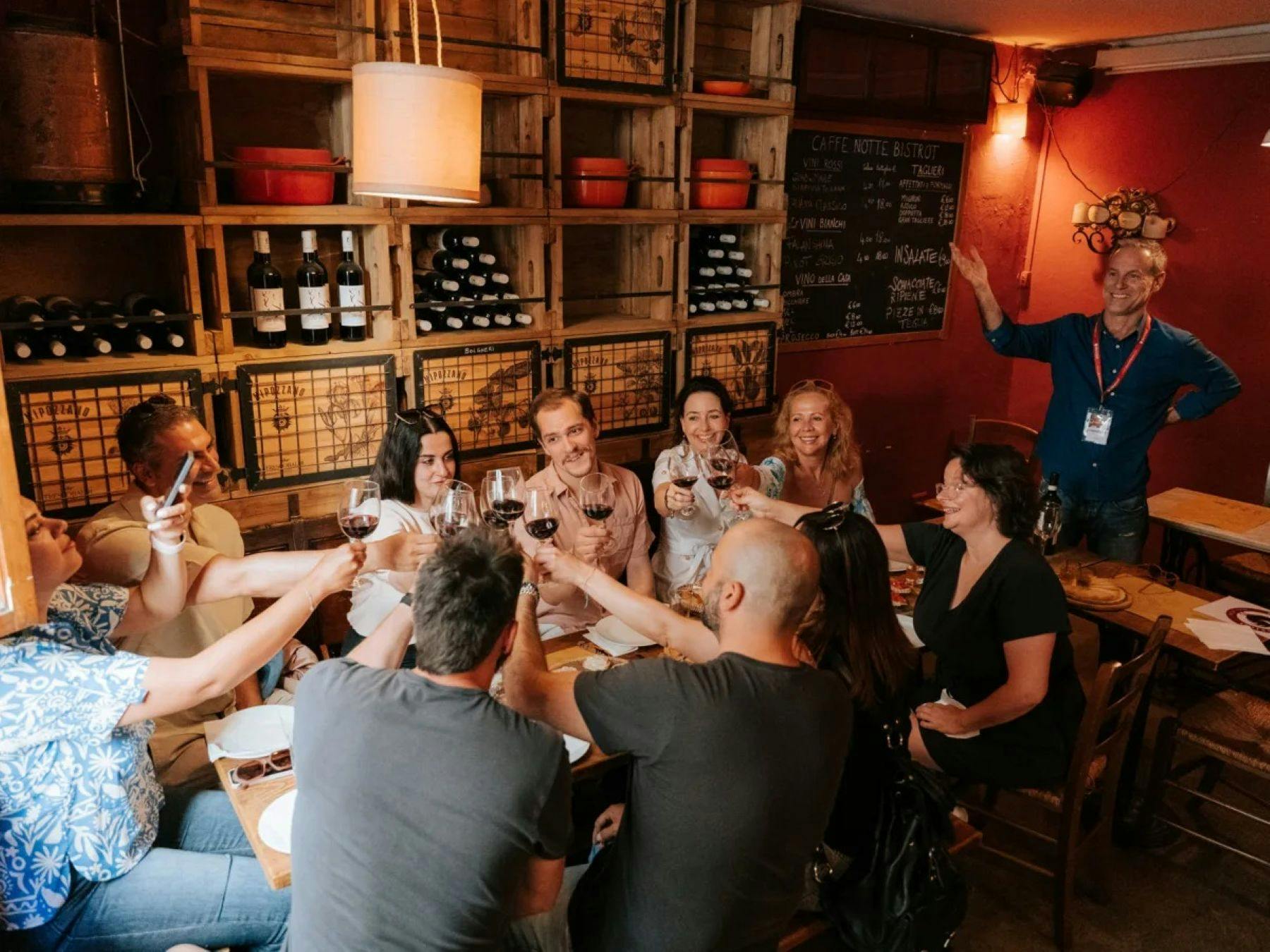 Un gruppo di persone sedute attorno a un tavolo in un ristorante accogliente, che brindano, con scaffali e decorazioni sullo sfondo.
