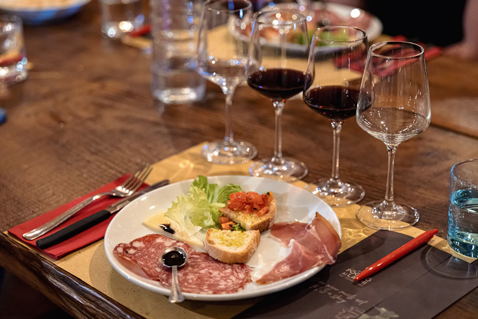 A plate with assorted appetizers, including cured meats and bruschetta, next to glasses of red wine on a wooden table.