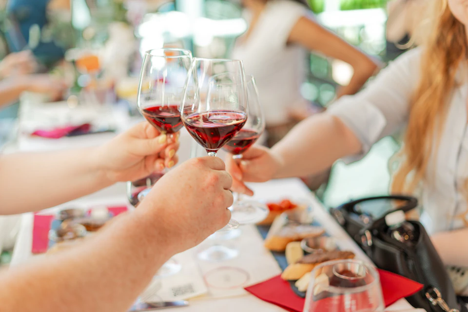 Three people clinking glasses of red wine over a table filled with various appetizers and snacks.