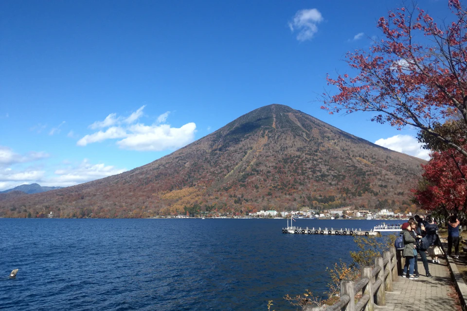 A scenic view of a lake with a wooden fence in the foreground, a mountain in the background, and a dock on the right.