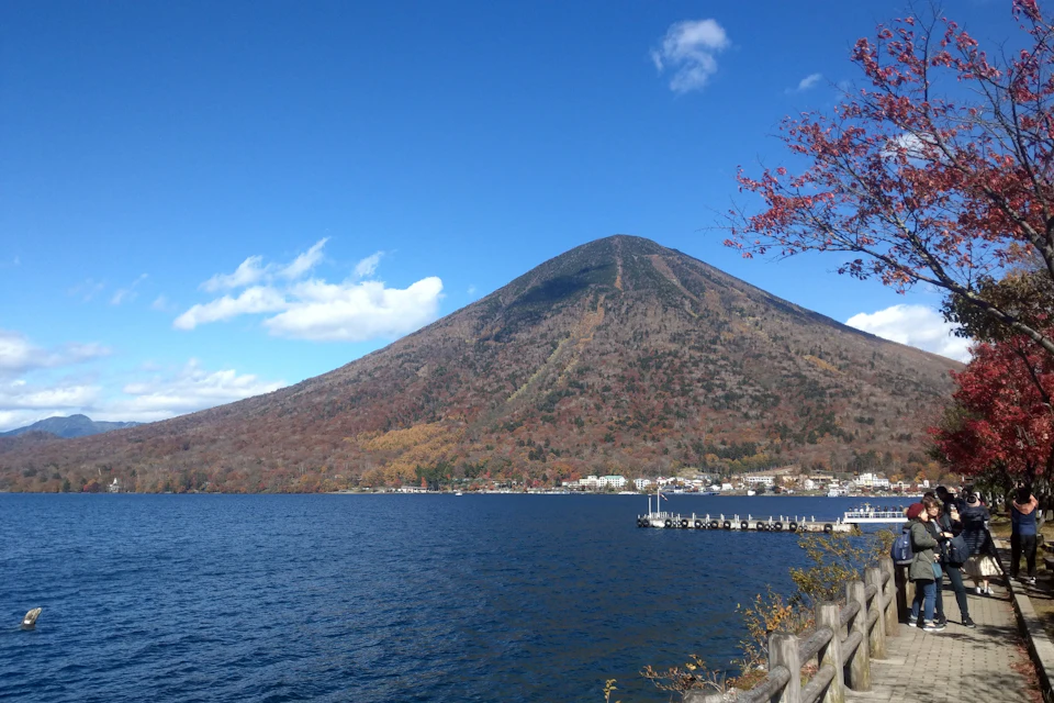 A scenic view of a lake with a wooden fence in the foreground, a mountain in the background, and a dock on the right.