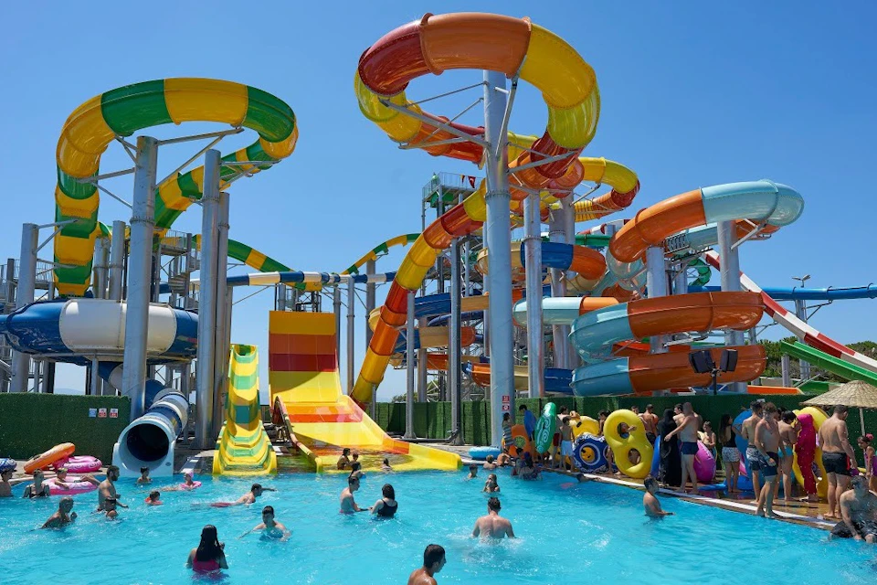 A water park with colorful slides and a pool filled with people enjoying the water under a clear blue sky.