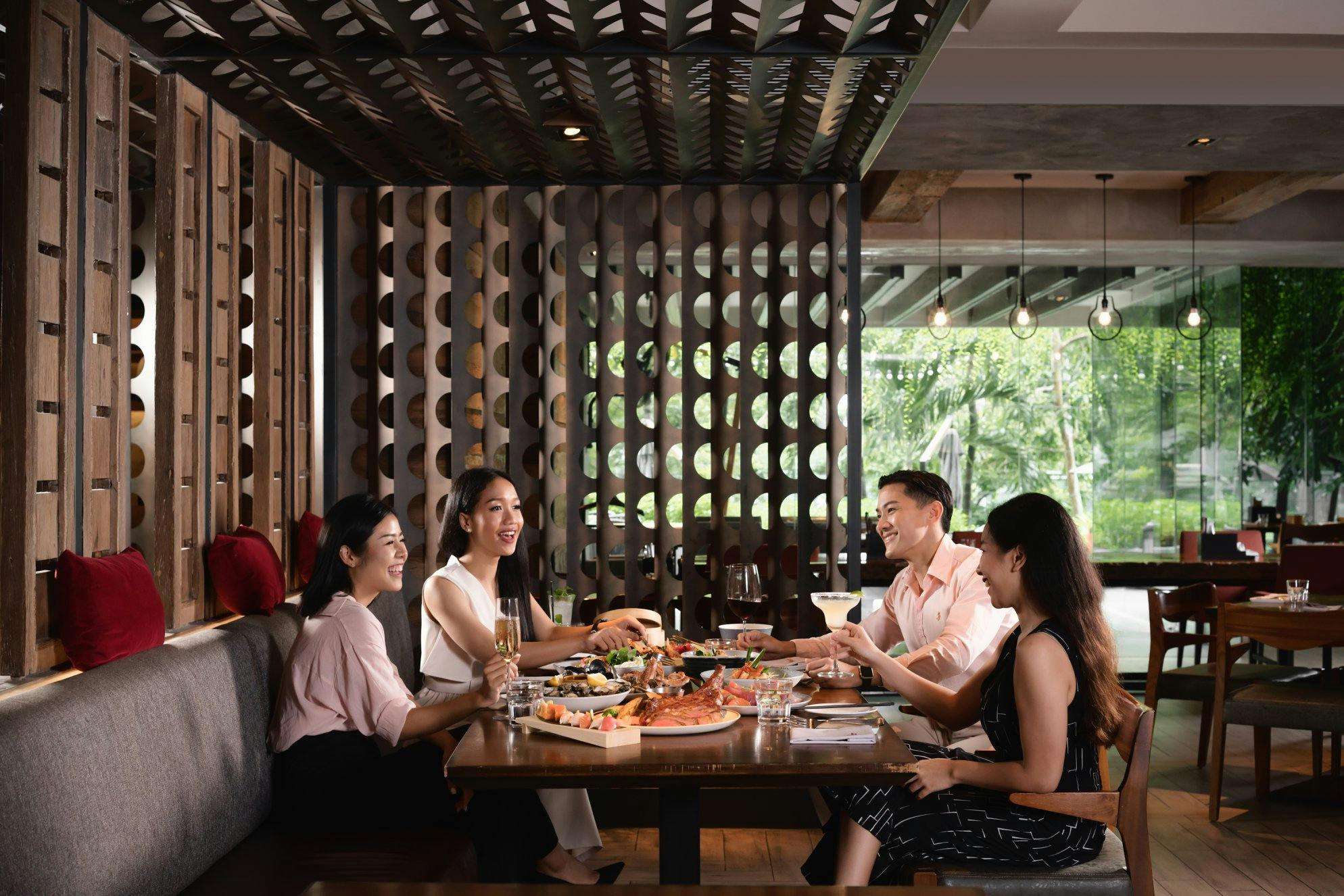 A group of people sitting at a restaurant table, enjoying food and drinks, with decorative wooden panels in the background.