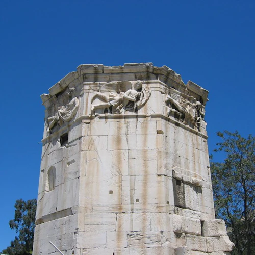 Åttakantigt stentorn med detaljerade sniderier på toppen, ställda mot en klarblå himmel, flankerad av träd.