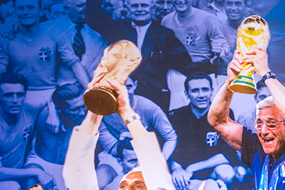 Wall mural with historical images of soccer players lifting trophies, plus modern memorabilia in an adjacent display case.