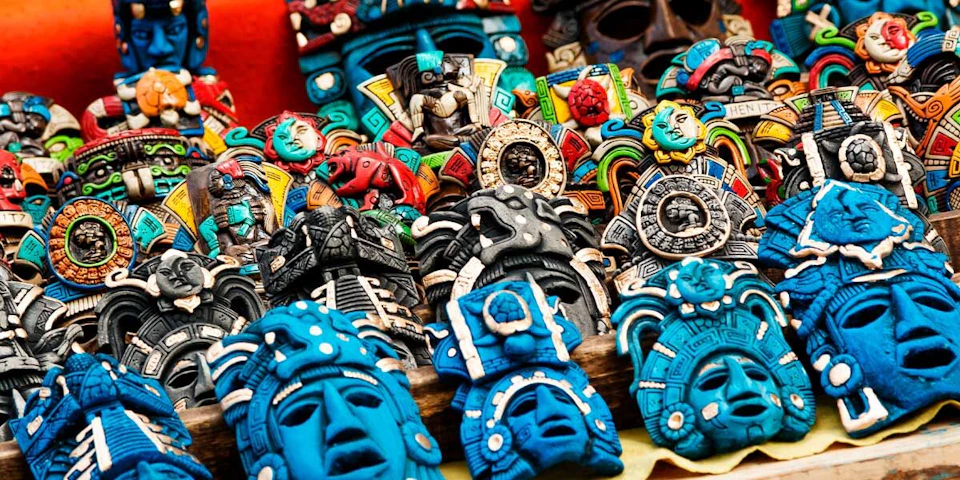 Colorful, intricately carved masks and figures in various designs and patterns, displayed closely together in a market setting.