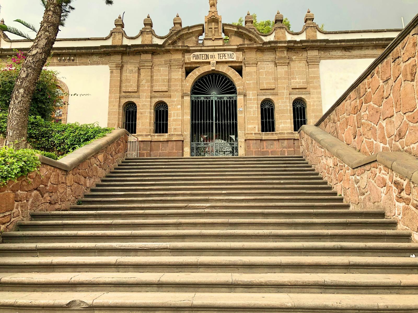 Kamenné schody vedou k ozdobné budově s klenutými okny a bránou. Na ceduli je napsáno „Panteon del Tepeyac“.