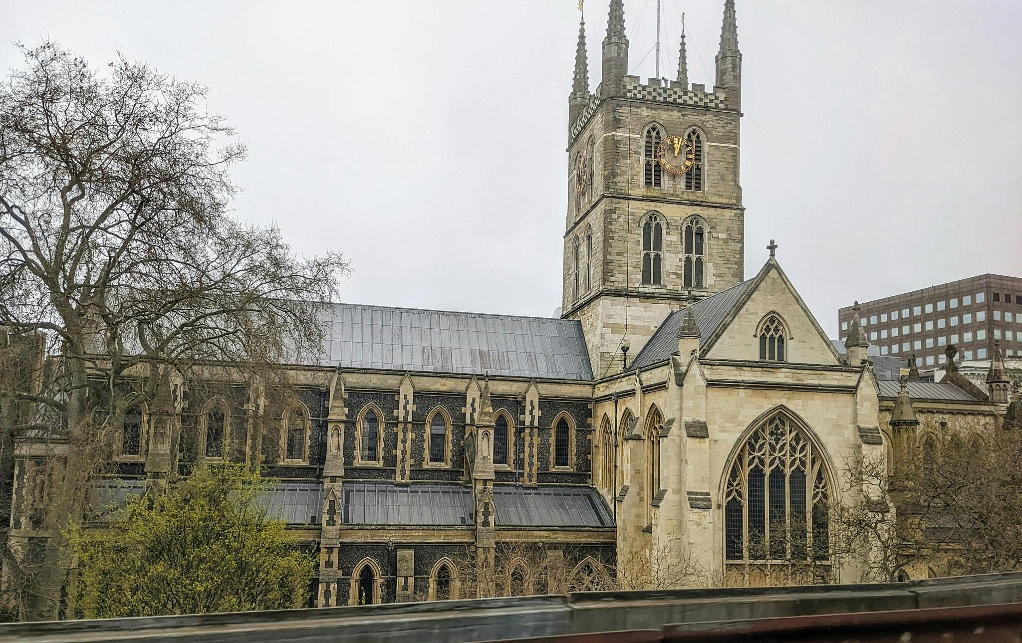 Uma grande igreja de estilo gótico com janelas intrincadas, uma torre de relógio alta e árvores nuas em primeiro plano.