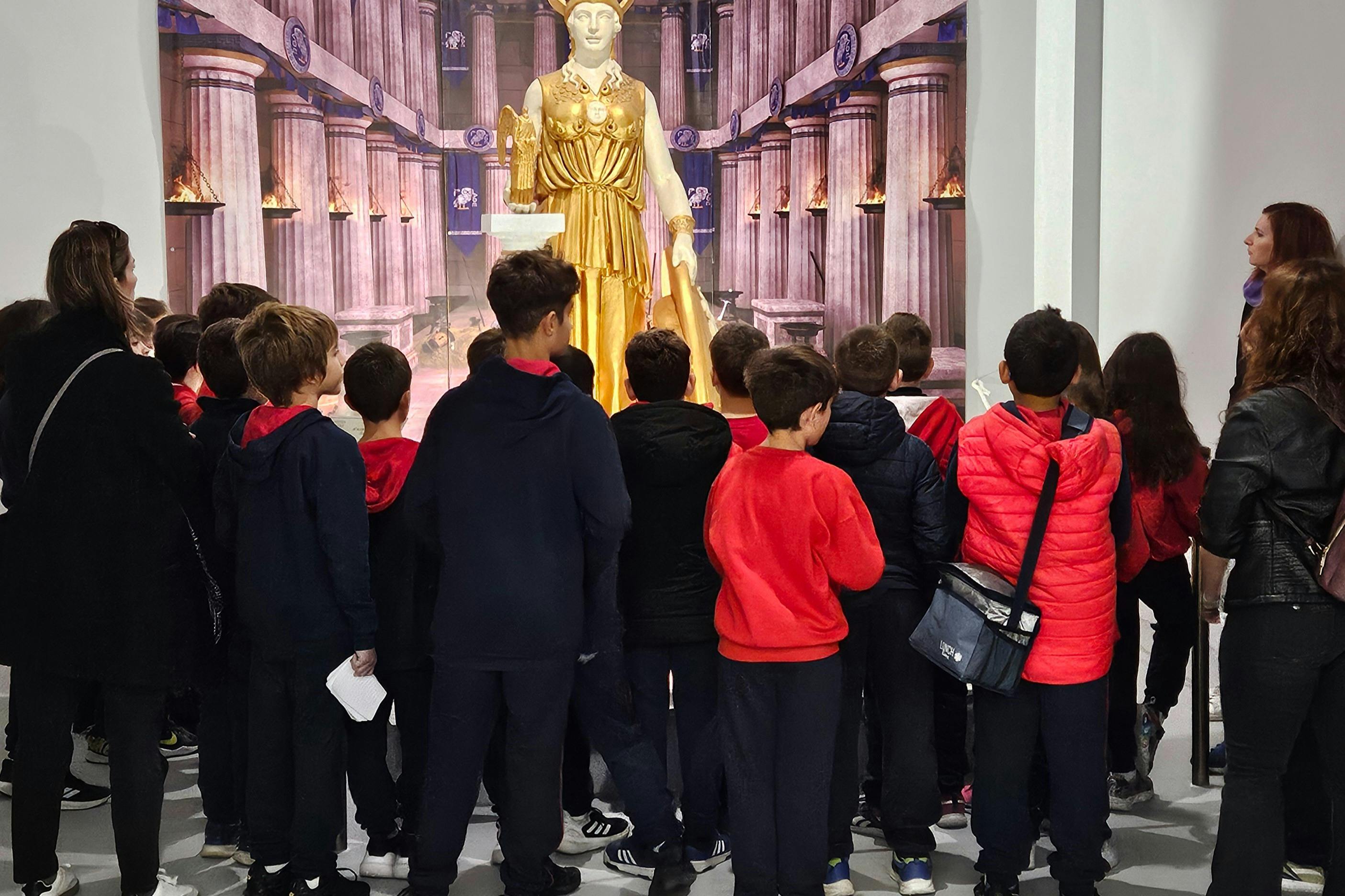 A group of children is gathered around a large, golden statue in a museum. An adult appears to be explaining the exhibit.