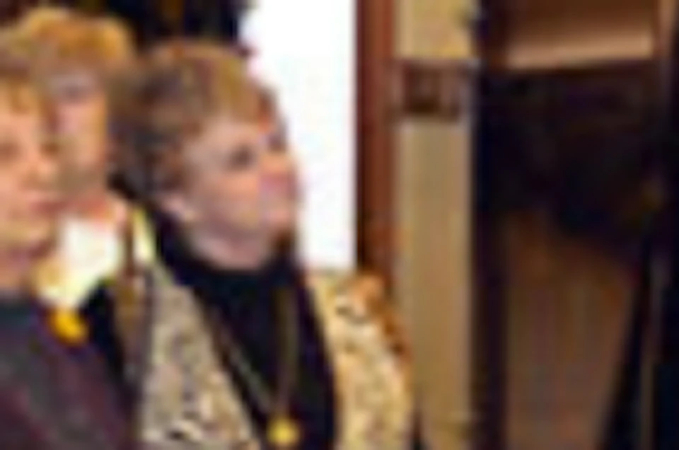 A group of elderly people stand in a museum, attentively viewing framed historical photographs of notable individuals on the wall.
