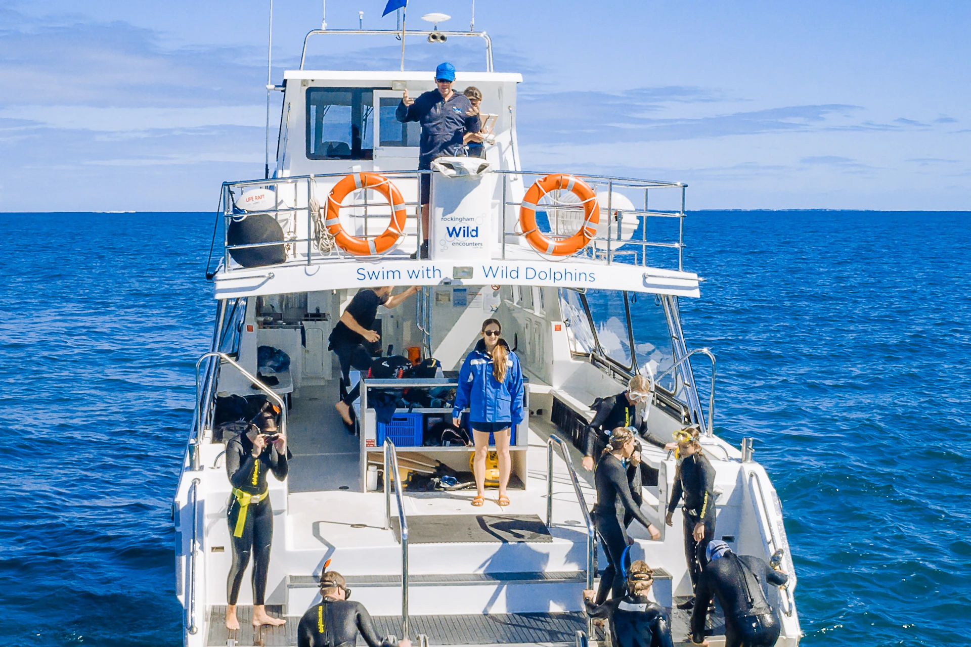 A boat labeled "Swim with Wild Dolphins" with people in wetsuits and snorkels preparing to enter the water.