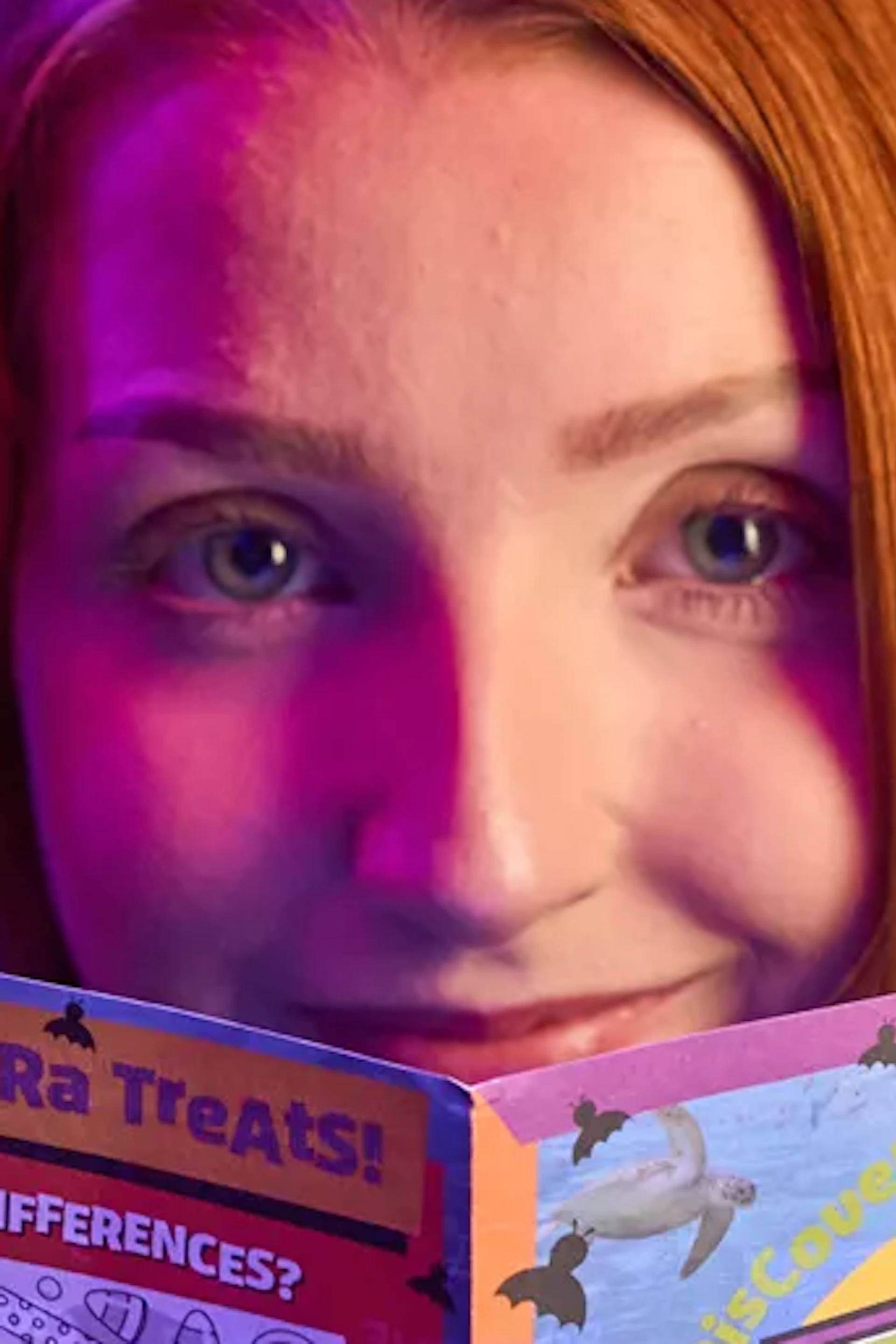 A person in a hoodie holds a colorful activity booklet titled "Tricks and Treats" with an aquarium backdrop.