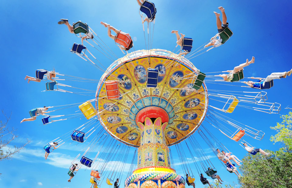A colorful swing ride in motion at an amusement park, with people seated and flying outward under a clear blue sky.
