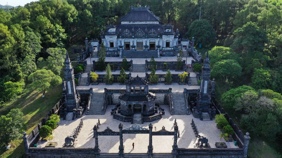 Aerial view of a historical stone temple with ornate architecture, surrounded by greenery and featuring a central courtyard.