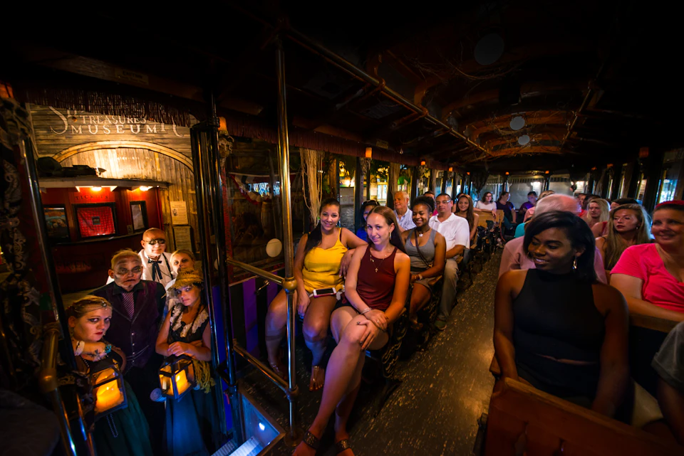 A group of people sitting on a train ride, smiling and enjoying a dimly lit, themed indoor attraction.