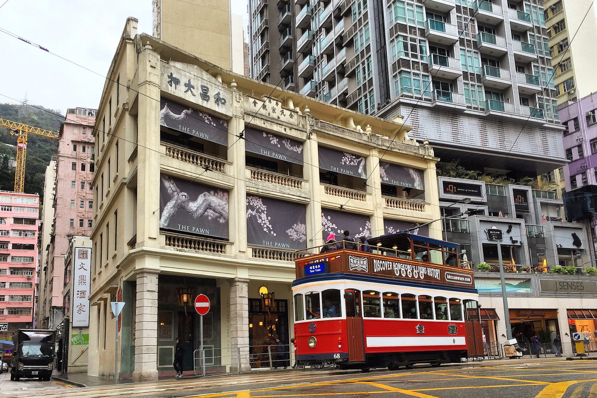 A vintage red and white tram passes in front of a historic building named The Pawn, with modern city buildings in the background.