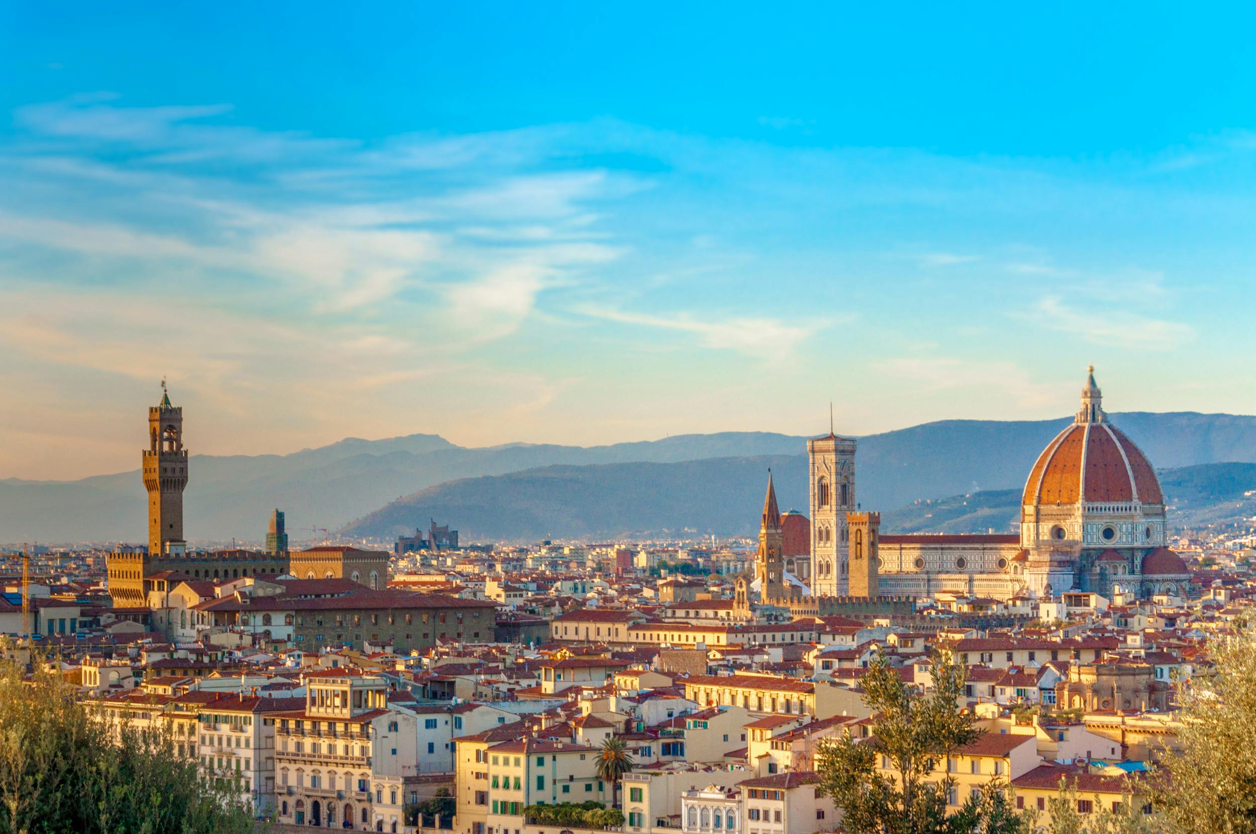 Panoramablick auf Florenz mit seinen historischen Gebäuden und ikonischen Kathedralen, unter einem klaren blauen Himmel mit fernen Bergen.