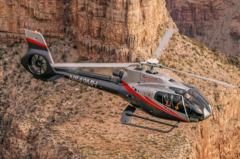 A helicopter flying near rocky cliffs in a canyon, labeled with "Maverick" and registration "N849MH."