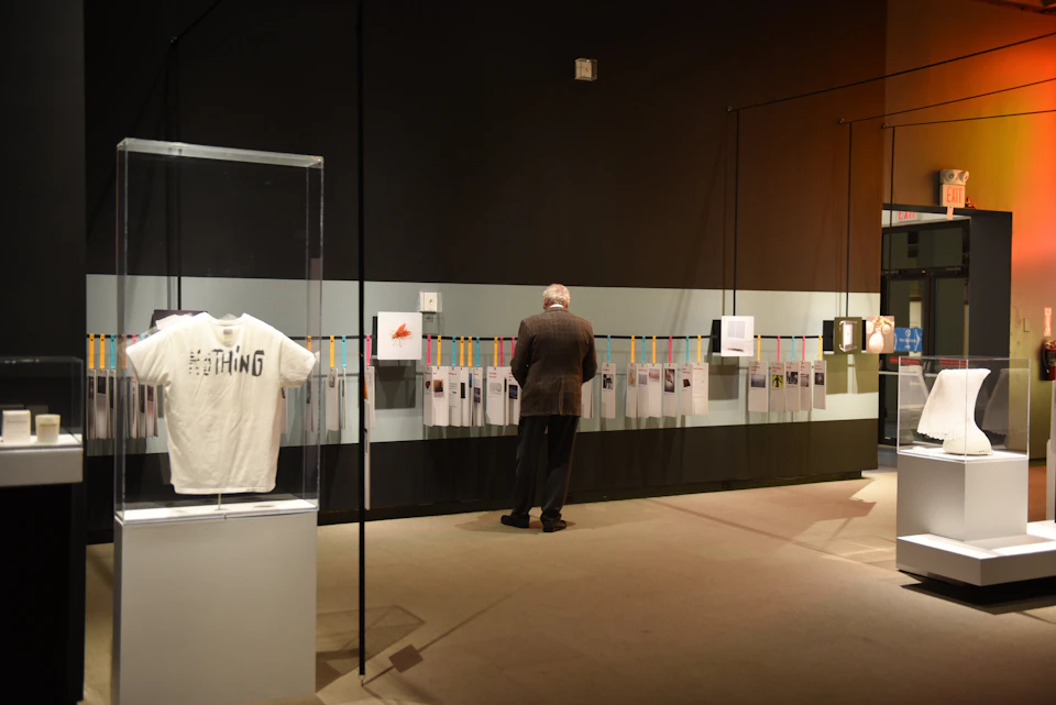 An older man in a museum examines a wall display of documents. A glass case with a t-shirt is visible in the foreground.