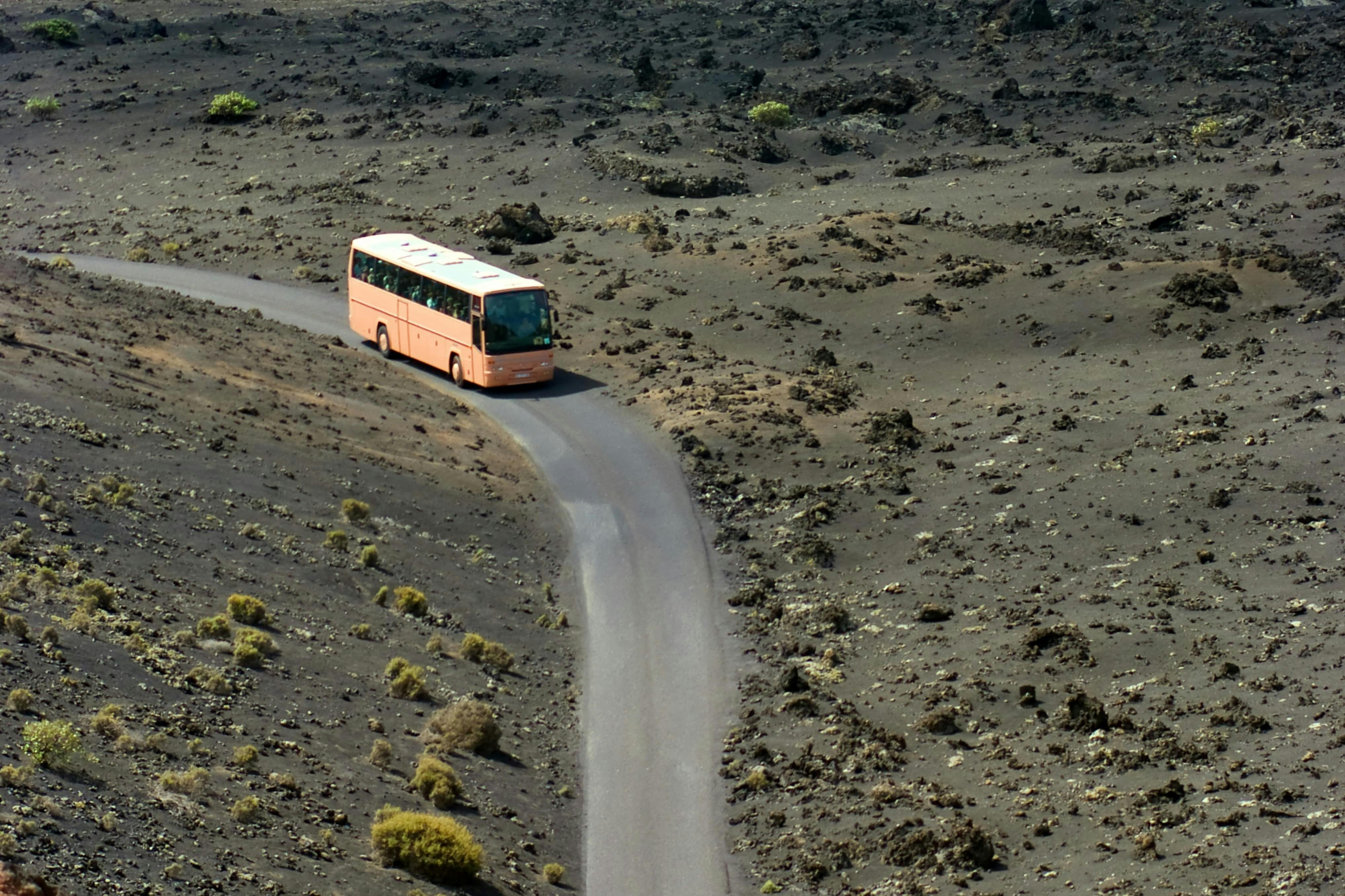 A peach-colored bus travels on a winding road through a barren, rocky landscape with sparse vegetation.