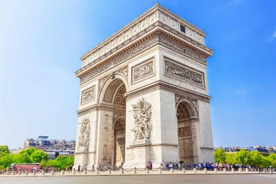 The Arc de Triomphe under a clear blue sky, with visible detailed carvings and a few people near its base.