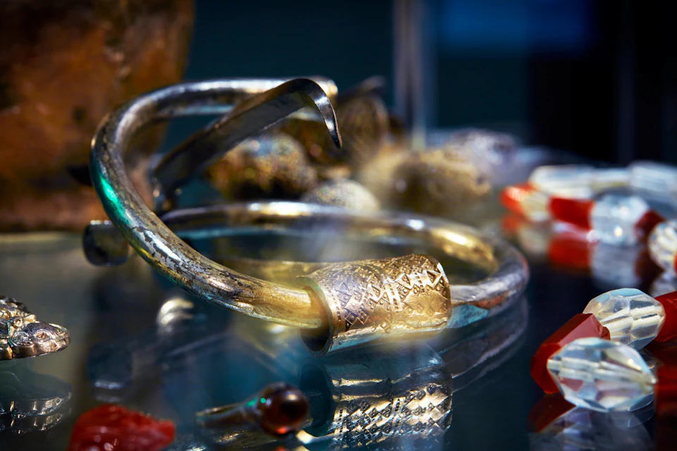 A close-up view of ornate metallic bracelets and decorative objects displayed on a reflective surface.