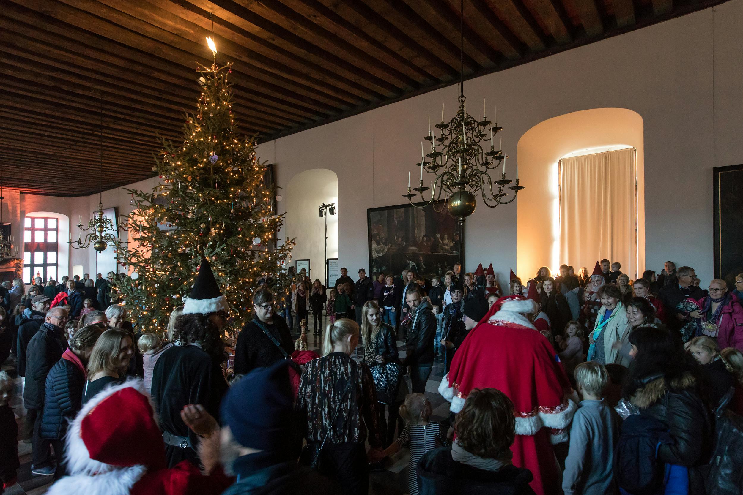 A large room filled with people celebrating Christmas near a tall decorated tree and a person dressed as Santa Claus.
