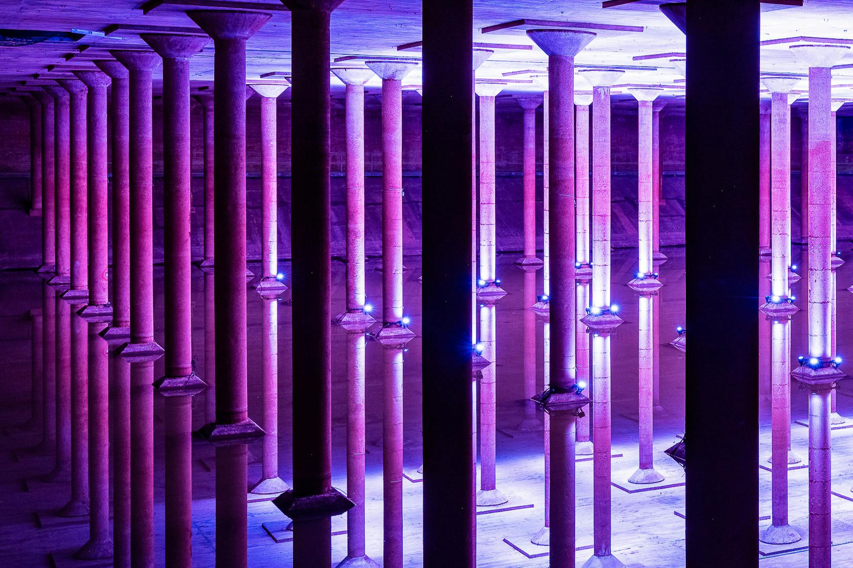 보라색과 파란색 조명으로 빛나는 수많은 기둥이 있는 대형 지하실은 정수면에 반사됩니다.