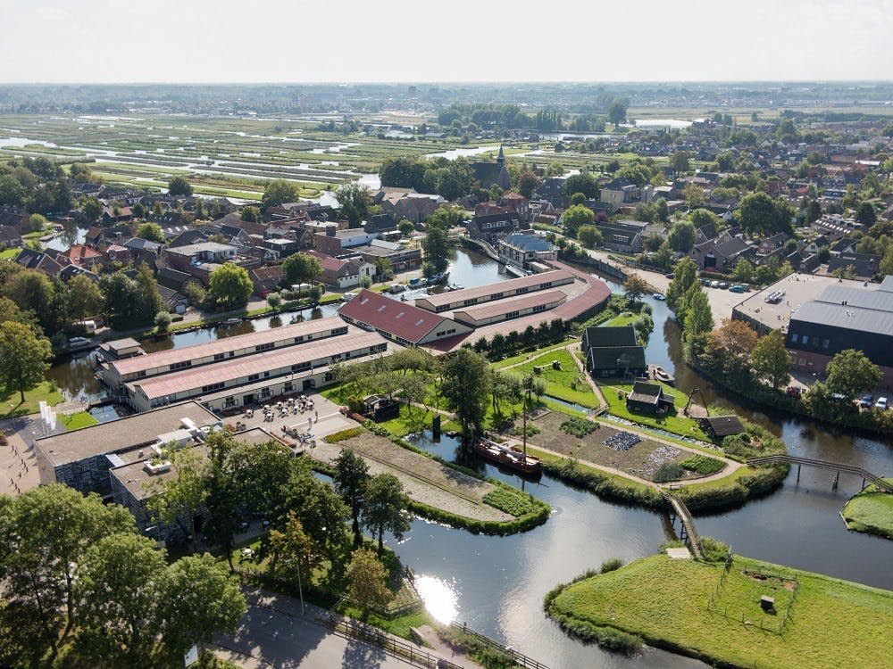 Aerial view of a town with canals, buildings, green spaces, and surrounding agricultural fields.